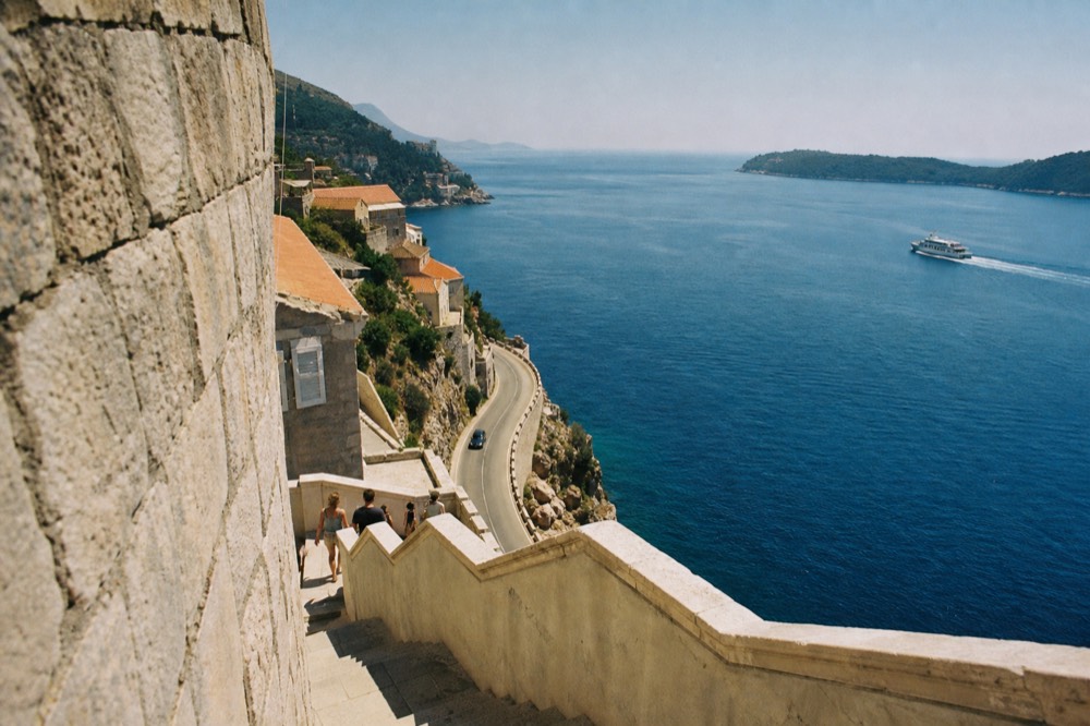 A coastal road winding along the Adriatic with a ferry in the distance