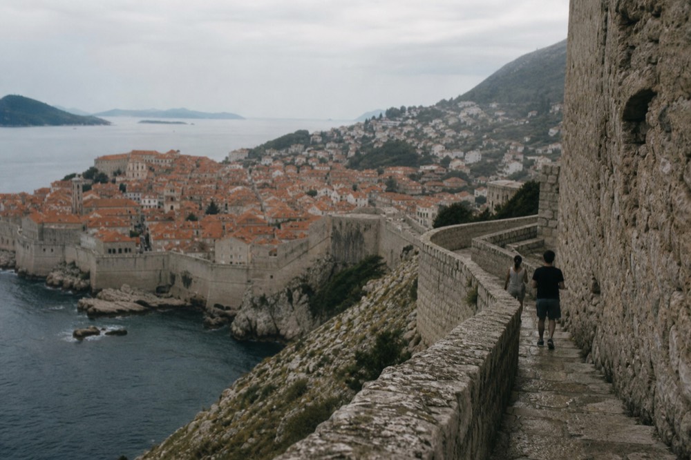 Walkers on the city walls path high above red rooftops of Dubrovnik