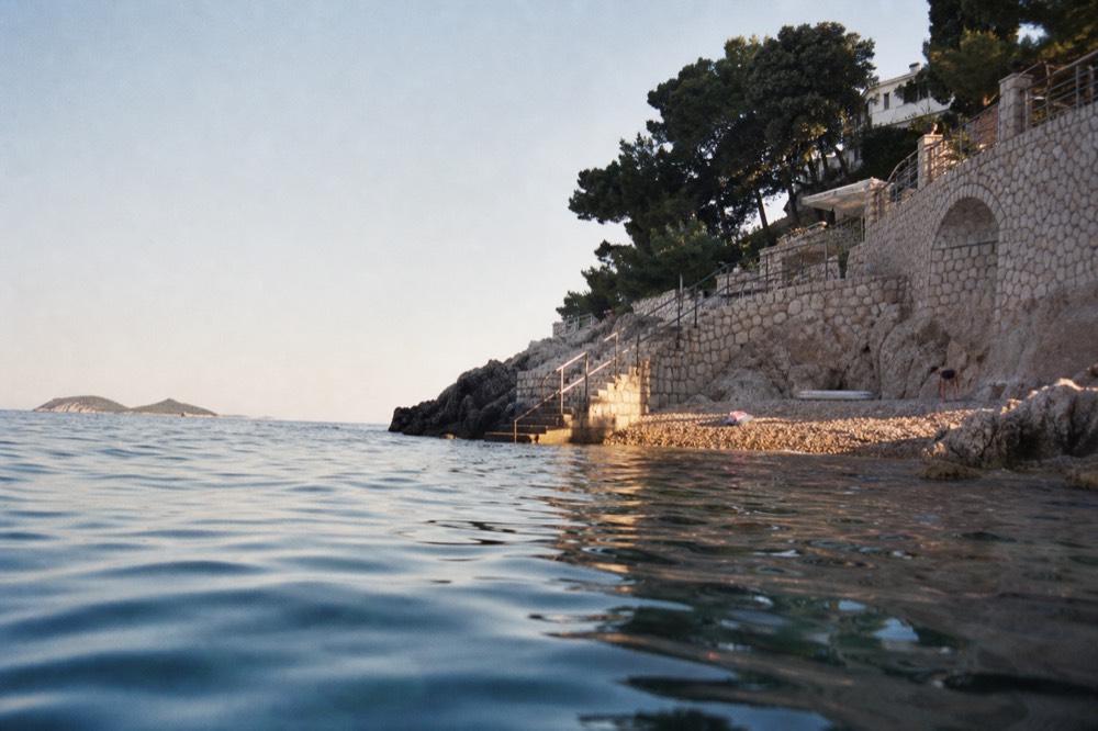 A coastal city in soft evening light with calm sea and distant islands