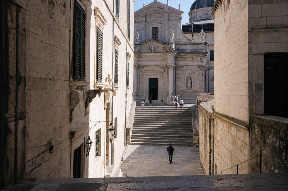 A wide stone staircase in Dubrovnik climbing toward a baroque church facade