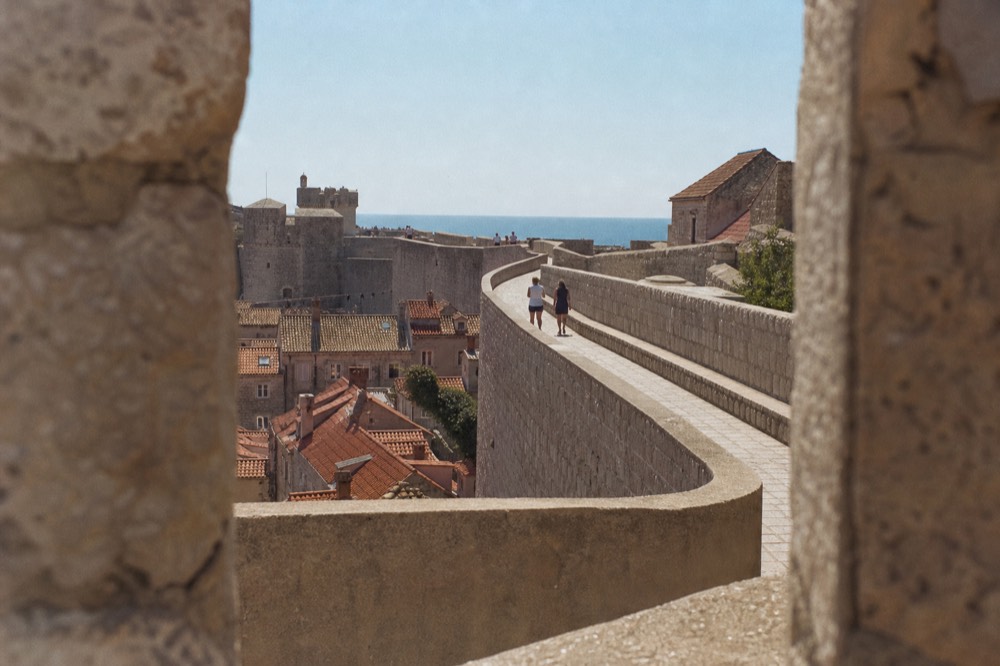 Walkers on the city walls path high above the red rooftops of Dubrovnik Old Town