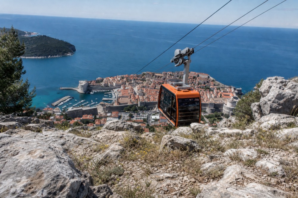 A cable car cabin ascending the hill above Dubrovnik with the walled city below