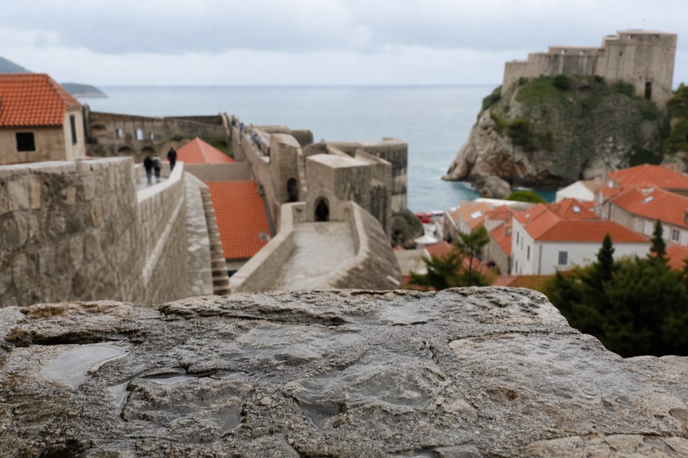The city walls of Dubrovnik curving above red rooftops toward the sea