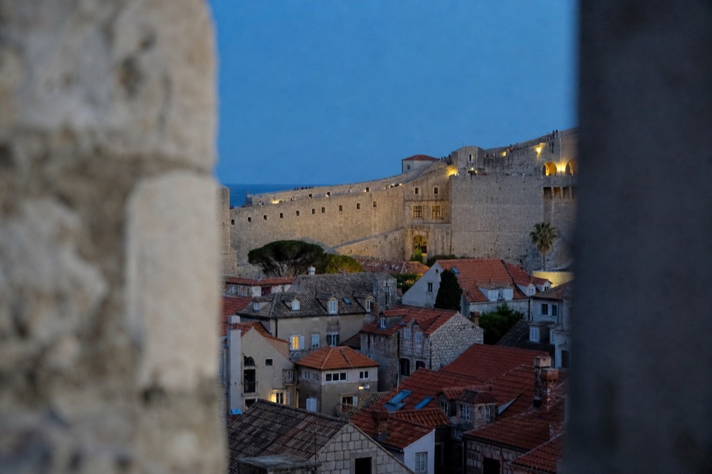 stone fortification wall rising above red rooftops of Dubrovnik