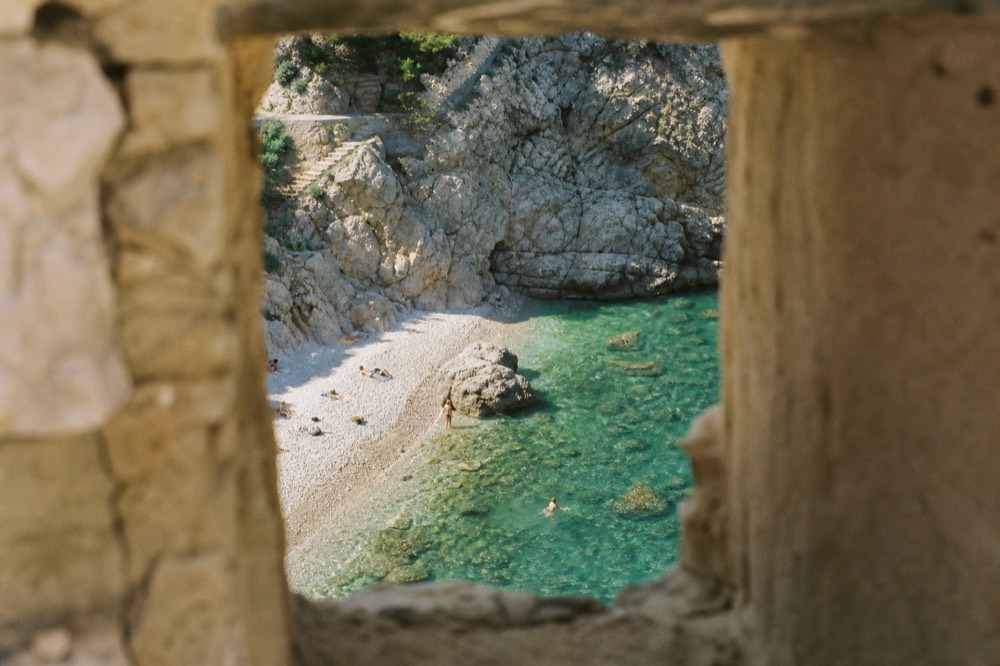 pebble beach with clear turquoise water below stone cliffs near Dubrovnik