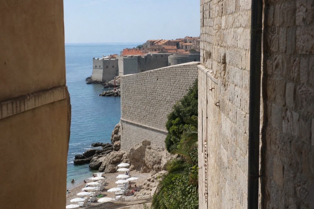 stone city walls curving above red rooftops toward the sea at Dubrovnik