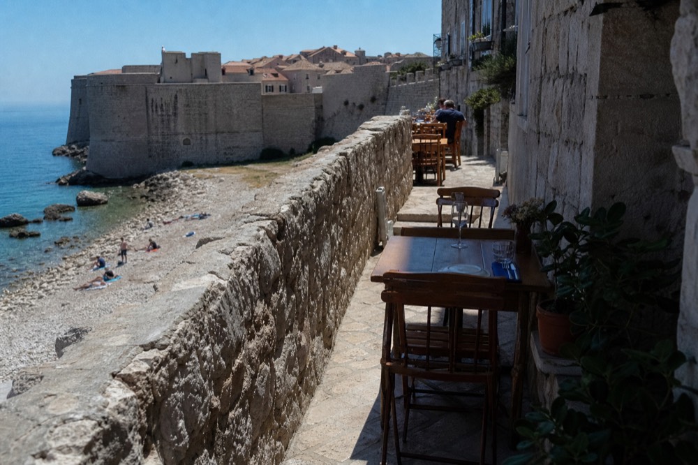 A small family konoba terrace with wooden tables set for dinner in a narrow stone street