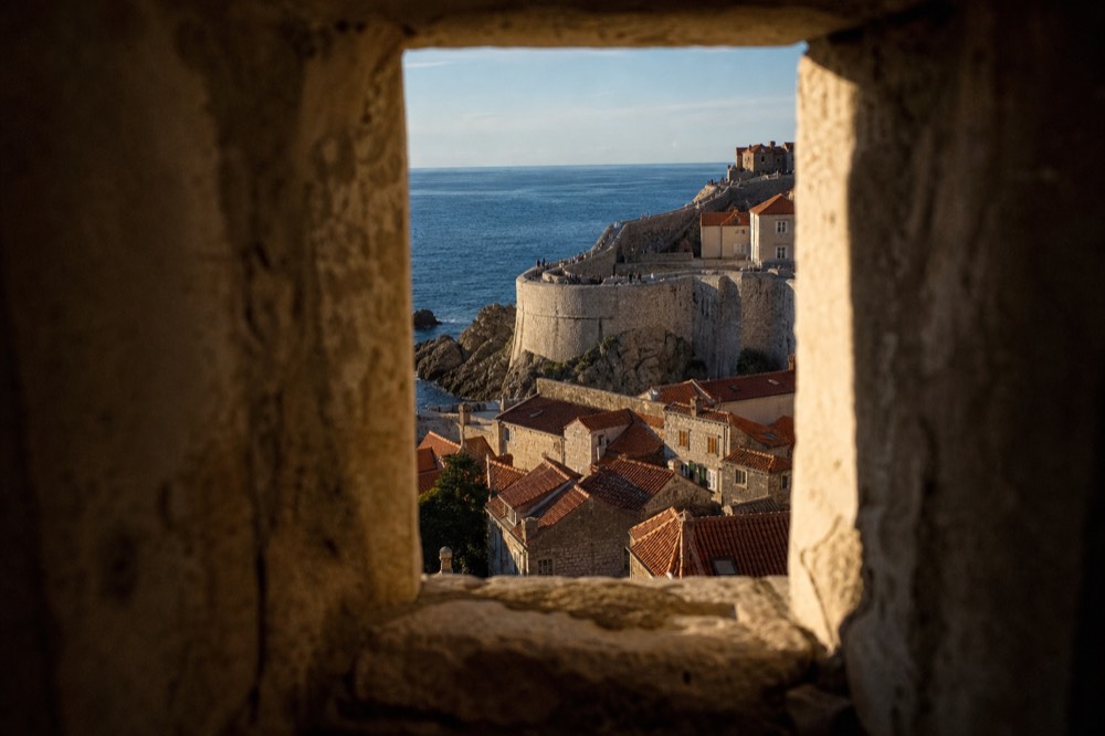 Stone city walls of Dubrovnik curving above red rooftops toward the sea