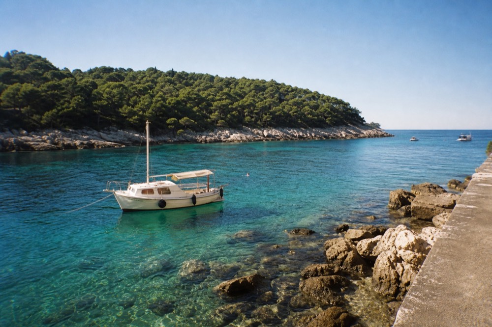Boat anchored in clear turquoise water near a wooded Adriatic island