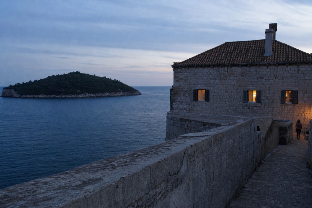 Stone fortifications rising above the sea with a wooded island in the distance