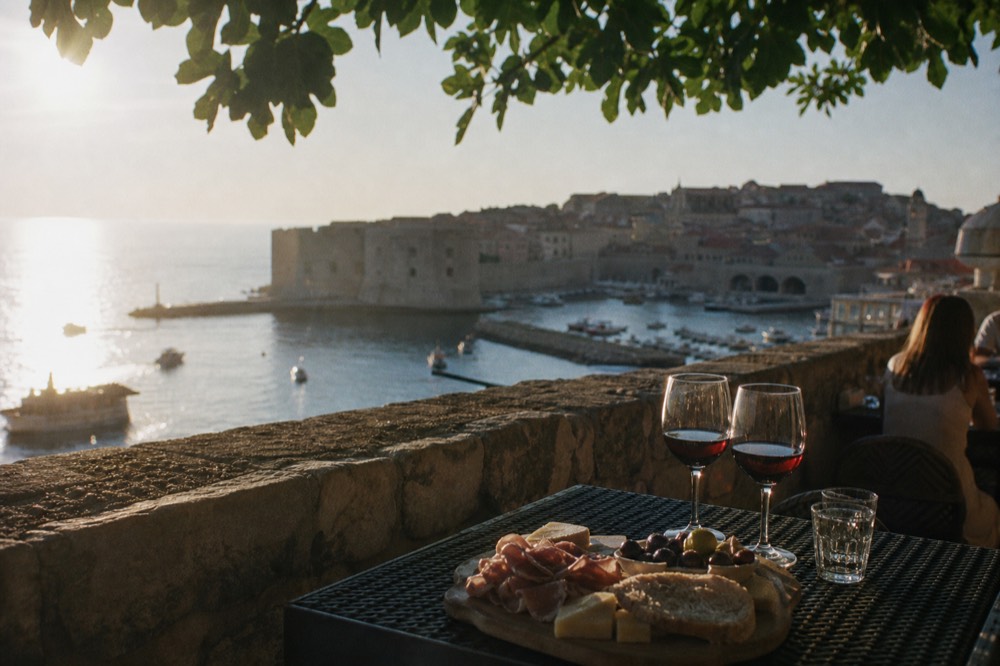 A tasting plate of prosciutto, cheese and bread beside glasses of red wine