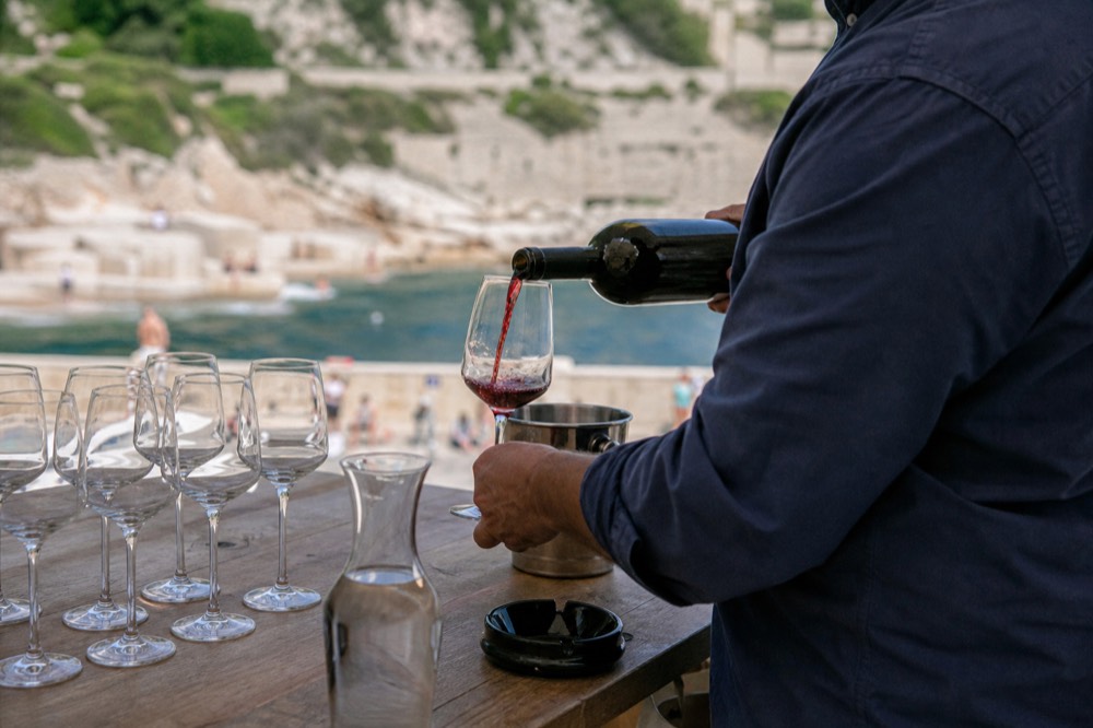 A winemaker pouring red wine into glasses at a wooden tasting table