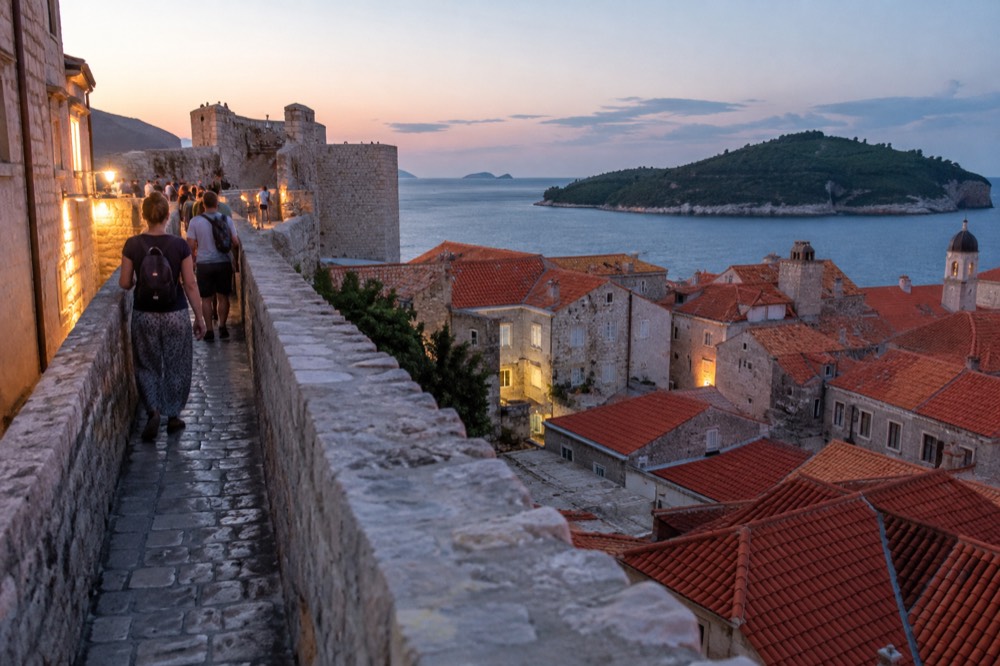 Walkers on the city walls above tiled rooftops and the sea