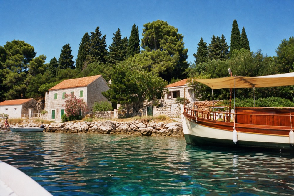 A wooden boat anchored beside a green Elaphiti island village with stone houses at the waterline