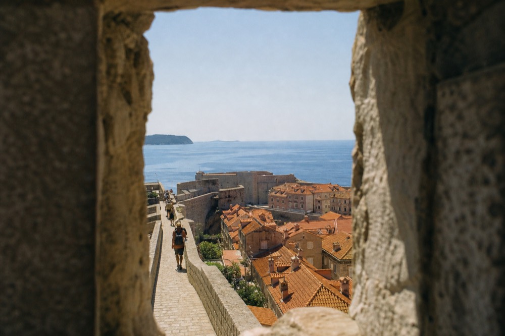 Stone walkway atop the Dubrovnik city walls with terracotta rooftops and the sea beyond