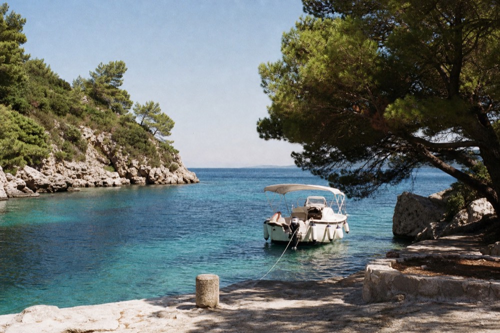 Small boat moored in a turquoise cove with pine trees and limestone cliffs on an Elaphiti island