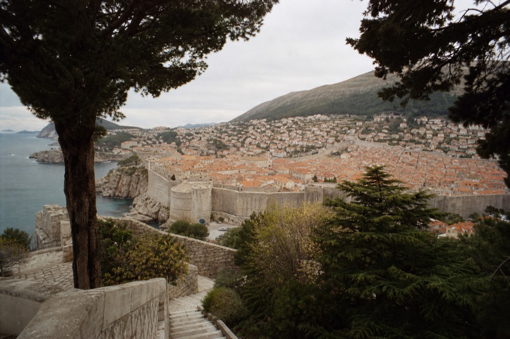 City walls of Dubrovnik curving above red rooftops under a grey sky