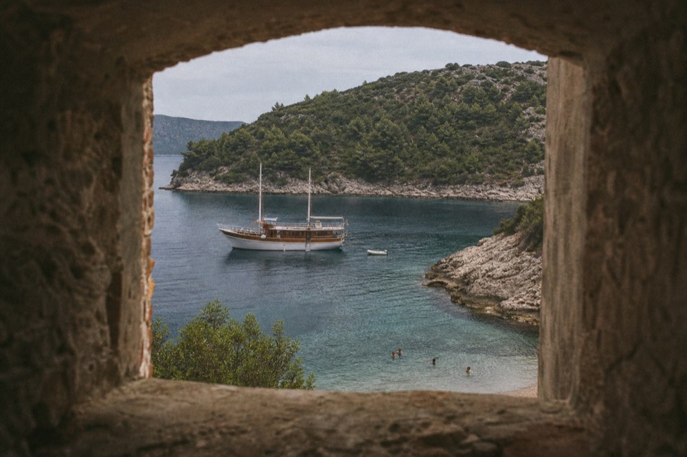 A wooden boat anchored in a small island bay with swimmers near the shore