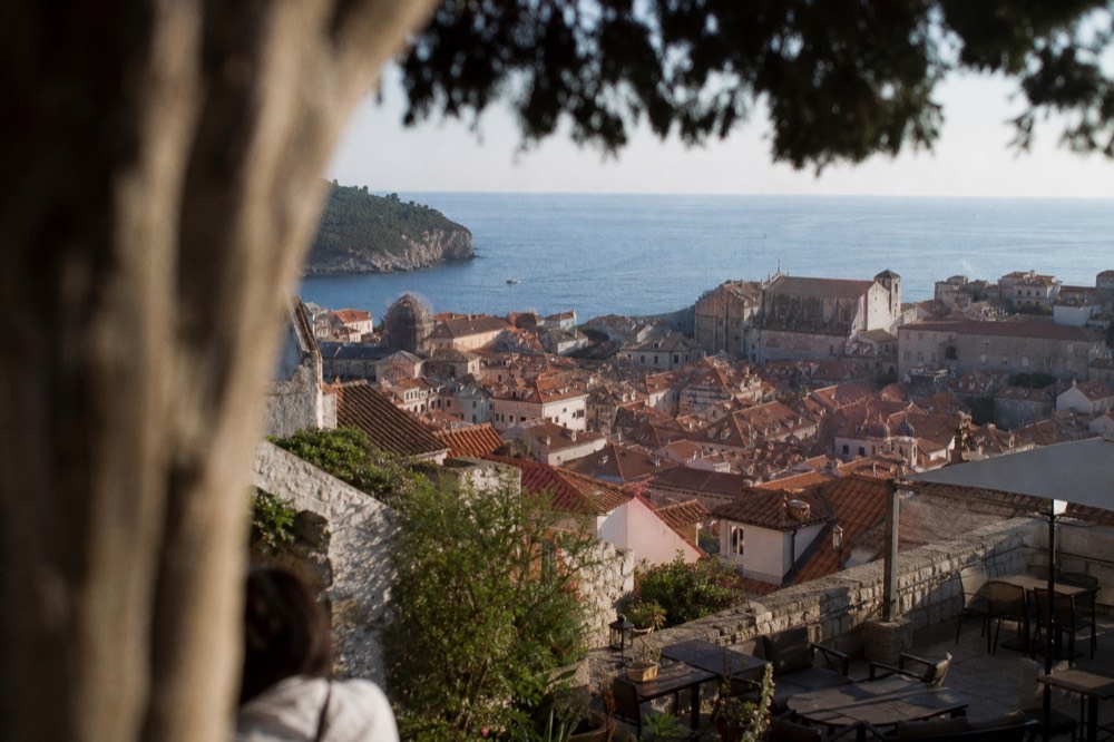 A quiet terrace above Dubrovnik with a view over terracotta roofs toward the sea at golden hour