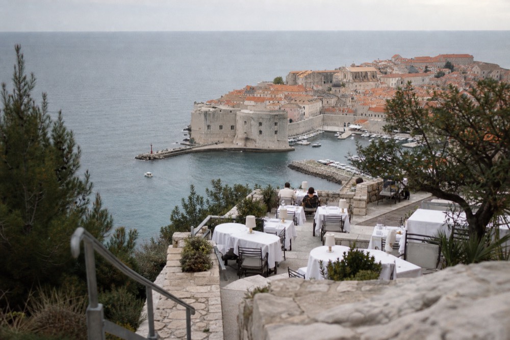A hotel terrace in Dubrovnik with white tablecloths overlooking the old harbour and city walls
