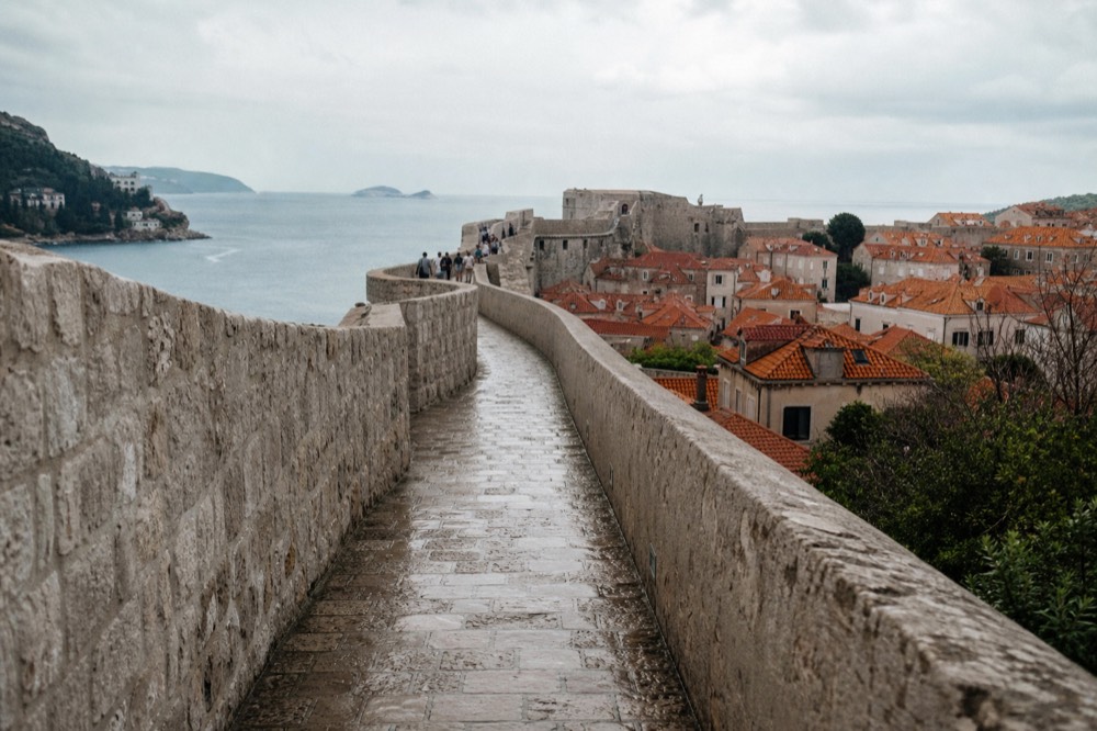 The city walls walkway curving above red rooftops toward the sea