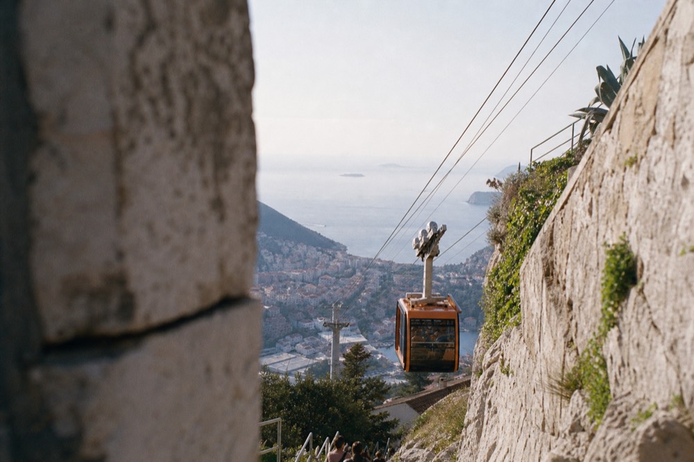 A cable car cabin ascending the steep cable above the coastline toward the hilltop station