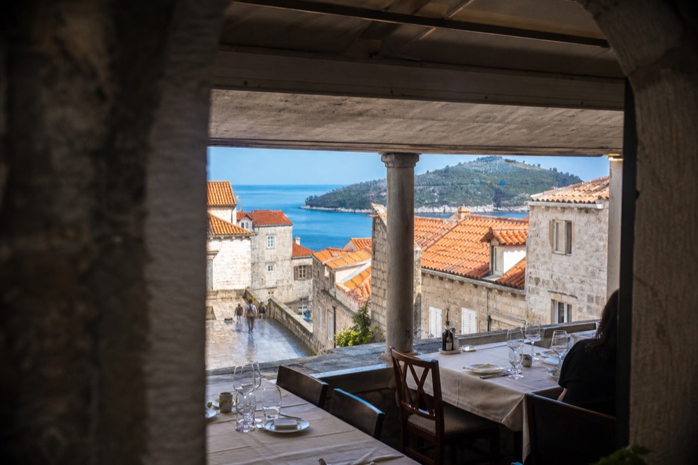 A covered restaurant terrace with set tables looking out at rain-washed stone streets